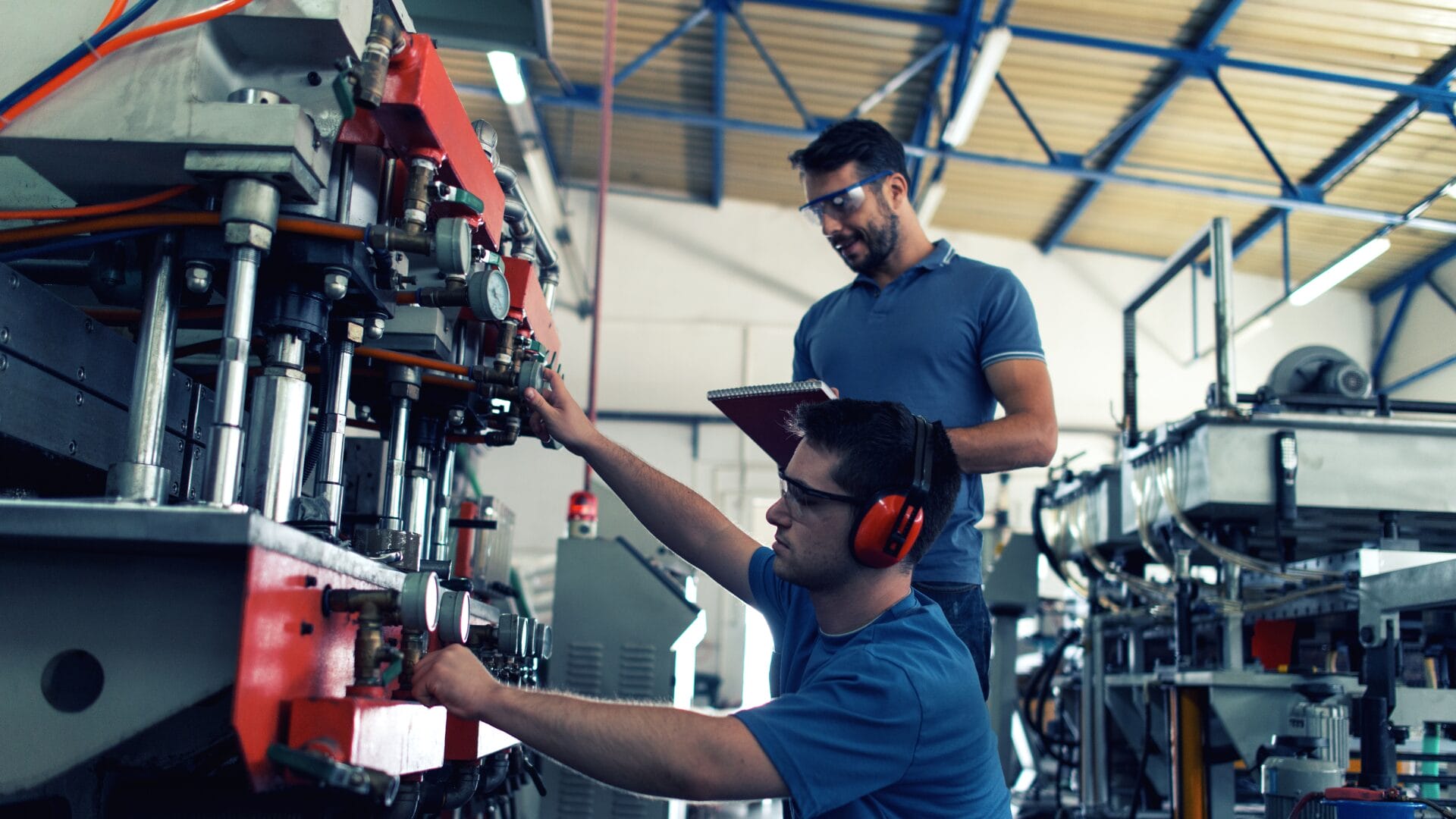 Two factory workers operating and inspecting automated manufacturing equipment in a smart factory setting.
