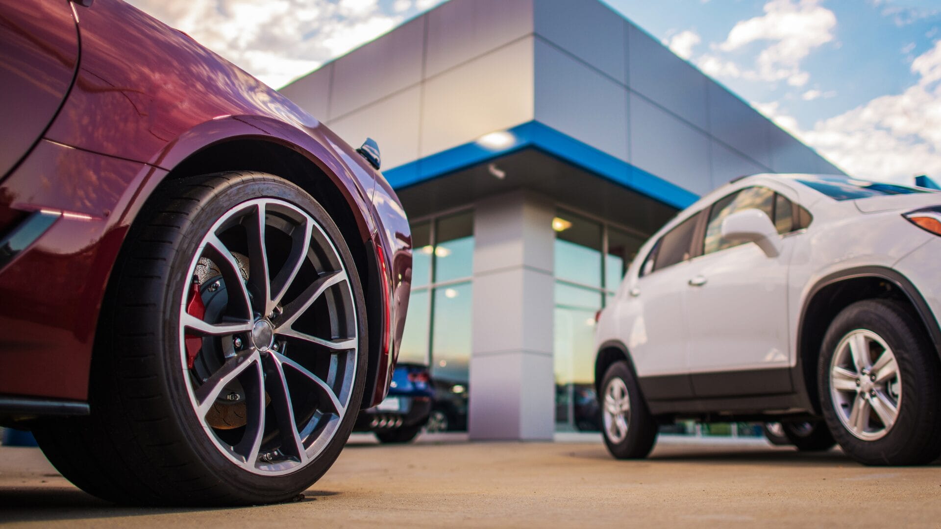 Close-up of red and white cars parked outside a modern dealership building, representing global automotive expansion and regional market presence.