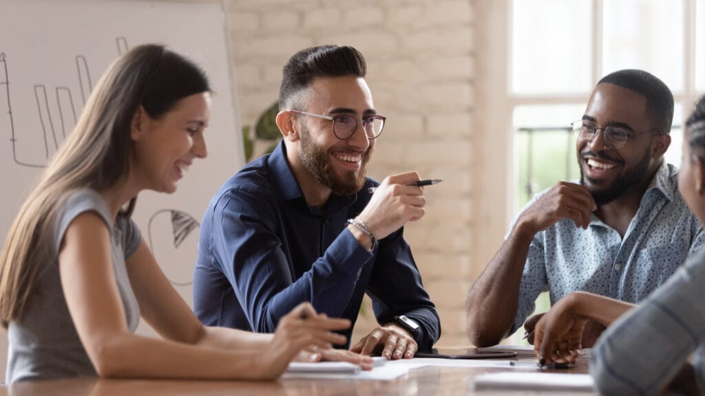 Group of diverse professionals smiling and discussing ideas around a table during a collaborative meeting, symbolizing community and knowledge sharing in the localization industry.