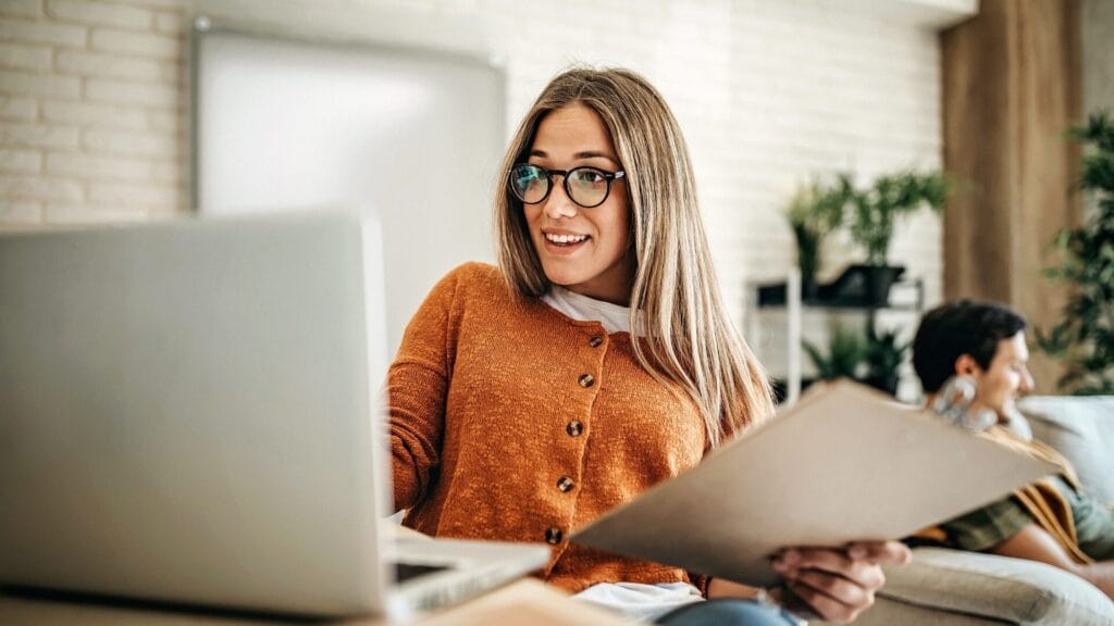 Woman using a laptop and reviewing documents at home, illustrating accessible and user-friendly digital workflows in a modern workspace