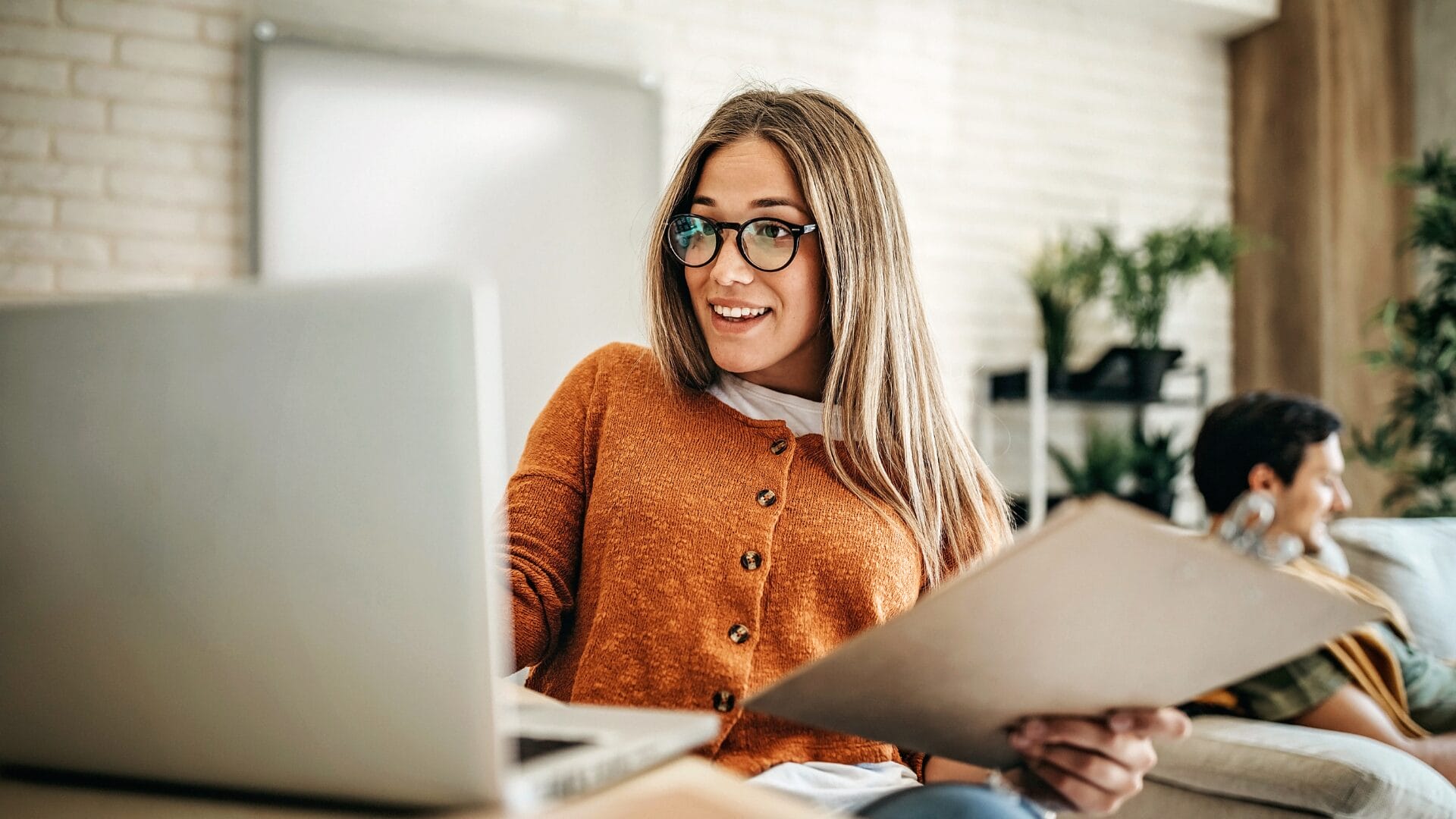 Woman using a laptop and reviewing documents at home, illustrating accessible and user-friendly digital workflows in a modern workspace