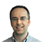 Professional headshot of smiling man with glasses wearing light blue shirt and gray sweater on white background